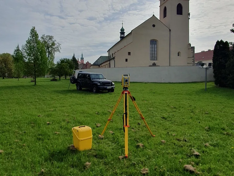 Totální stanice na stativu při zaměřování kostela s věží